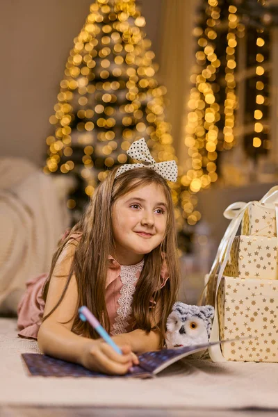 メリークリスマスとハッピーホリデー かわいい子供の女の子は屋内でクリスマスツリーの近くにサンタクロースに手紙を書きます — ストック写真