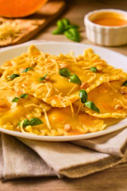 Ev yapımı balkabağı Ravioli, ricotta peynirli fesleğen, çam fıstığı ve sert peyniri ahşap masa malzemeleriyle çevrili beyaz tabakta servis ediyor. Seçici odak.