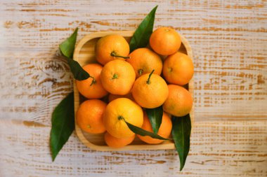 Mandalinalar - portakallar, mandalinalar, mandalinalar, ahşap arka planda yaprakları olan turunçgil meyveleri, çelenklerle süslenmiş noel kompozisyonu