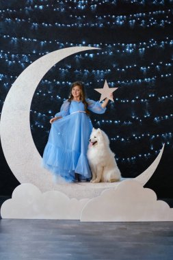 Açık mavi elbiseli güzel küçük kız, bulutların üzerinde beyaz Samoyed köpeğiyle kal. Stüdyoda harika bir fotoğraf.