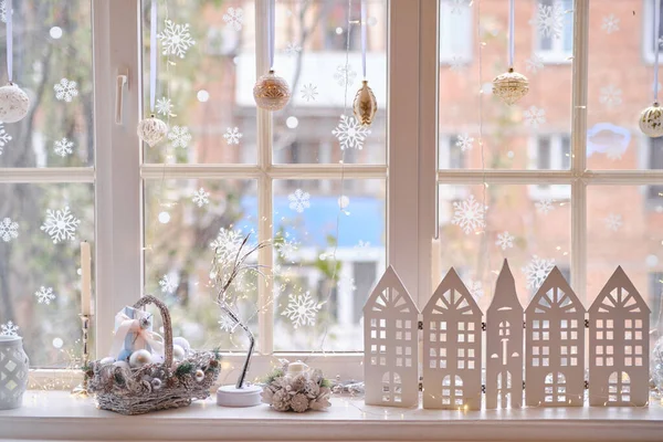 winter decor on windowsill with decor, basket with Christmas balls, wooden houses, candles and lights