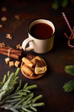 Yeşil ladin dalları, tarçın, kurabiye ve baston şekerler arasında Noel süslemeleri ile çevrili bir fincan sıcak çikolata, koyu bir arka plana karşı. Isıtıcı içecek. Xmas huysuz.