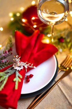 Geleneksel Noel masası kapanıyor. Altın çatal bıçak takımı, geyik yüzüklü keten peçete, ladin dalları ve bir bardak şarap. Tatil geçmişi. Seçici odak, çelenk, bokeh.