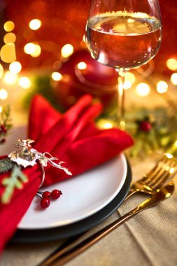 Geleneksel Noel masası kapanıyor. Altın çatal bıçak takımı, geyik yüzüklü keten peçete, ladin dalları ve bir bardak şarap. Tatil geçmişi. Seçici odak, çelenk, bokeh.