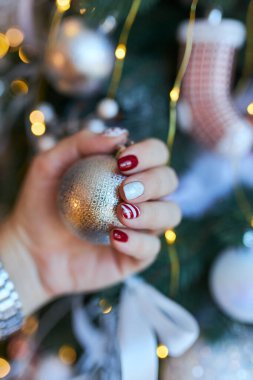 Yılbaşı manikürü, soyut tırnak tasarımı. Manikürlü güzel bir kadının eli Noel ağacının arka planında.