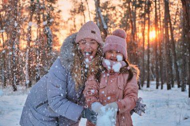 Anne ve Çocuk kışın karla oynuyorlar. Noel 'de kış parkında örgü şapkalı bir aile kar taneleri yakalıyor. Çocuklar için kar topu savaşı.