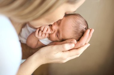 Uyuyan bebeğin başını tutan ve tatlı, tapılası bebeğini öpen mutlu genç annenin yakın çekimi. Ev çekimi, konsept bakım.