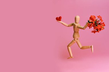 Büyük bir buket kırmızı çiçekli ve pembe arka planda kalbi olan ahşap bir manken. Teklif, nişan, ilan-ı aşk, Sevgililer Günü veya Anneler Günü.