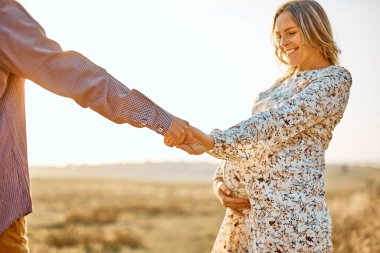 Koca göbekli hamile koca yaz güneşli havalarda dinleniyor. Mutlu çiftin birbirine aşık olduğu beyaz erkek ve kadının el ele tutuşması.