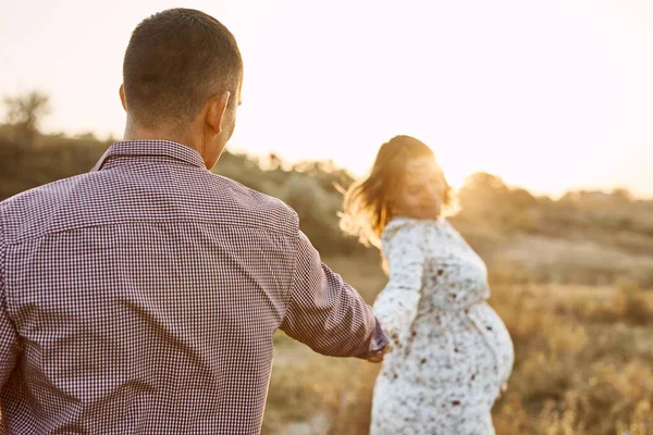 お腹の大きい妊婦さんとご主人は夏の晴れた日に川のほとりで休んでいます 幸せなカップルで愛Caucasian男と女抱擁手屋外 — ストック写真