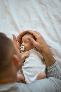 Tanımlanamayan bir babanın kucağında uyuyan bir bebeğin kafasını tutması, yatakta uyuması. Emin ellerde.