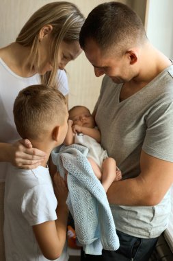 Baba ve anne kucağında yeni doğmuş kızı, yanında duran ağabeyi sevgiyle bakıyor. Aile değerleri