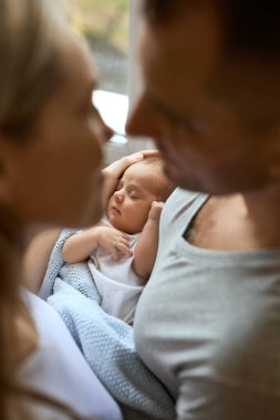 Yeni doğmuş bebeklerini kucağında tutan, sevgiyle bakan tanınamayan ebeveynlerin yakın portresi.