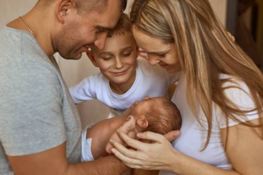 Baba ve anne kucağında yeni doğmuş kızı, yanında duran ağabeyi sevgiyle bakıyor. Aile değerleri