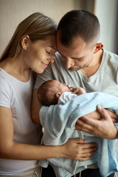 Kadın ve erkek yeni doğmuş bir bebeği tutuyor. Anne, baba ve bebek. Yakın plan. Ellerinde yeni doğmuş bir bebekle gülümseyen genç bir ailenin portresi..