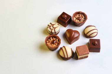 Yukarıdan bakıldığında, beyaz arka planda çeşitli çikolata şekerleri. Daire şeklinde uzanan farklı zevklere sahip lezzetli tatlılar. Yemek kavramı, tatlı..