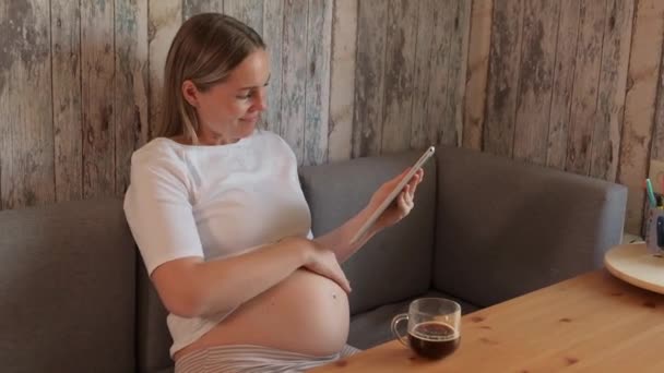 Urocza Kobieta Ciąży Pije Kawę Patrzy Ekran Tabletu Ciąża Technologia — Wideo stockowe