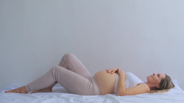 Pełnowymiarowa Kobieta Ciąży Leży Jasnym Łóżku Przytulając Brzuch Tle Jasnej — Wideo stockowe