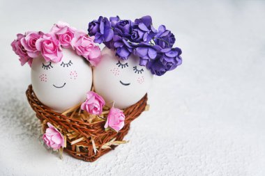 Sıcak bir Paskalya sepetinde duran çiçekli bahar çelenkleriyle tatlı yüzlü iki Paskalya yumurtası. Kopya alanı ile Paskalya için yaratıcı kartpostal