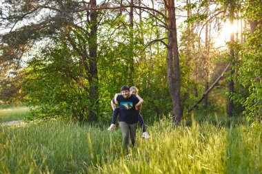 Father giving piggyback ride to small daughter on a walk in summer forest.