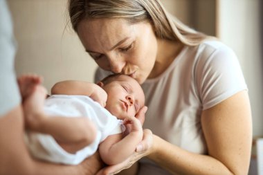 Mutlu, genç bir annenin yeni doğmuş bebeğini kucağına alıp tatlı, tapılası bebeğini öpmesi. Ev çekimi, konsept bakım.