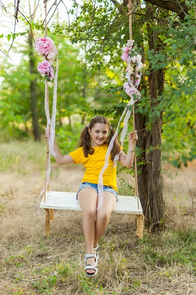 黄色のTシャツのかわいい笑顔の女の子は 木の森の中でスイングを楽しんでいます 晴れた日 子供のための夏の屋外活動 — ストック写真