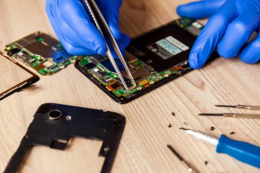 The technician repairing the smartphones motherboard in the workshop on the table. Concept of mobile phone, electronic, upgrade and technology.
