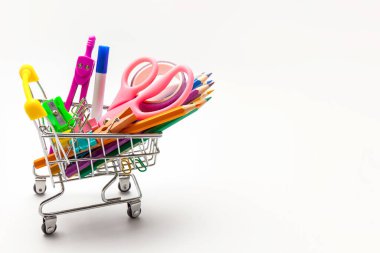 Beyaz arka planda izole edilmiş çok renkli okul malzemeleriyle dolu bir alışveriş arabası. Okul konseptine dönelim.