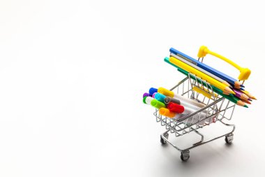 Beyaz arka planda izole edilmiş çok renkli okul malzemeleriyle dolu bir alışveriş arabası. Okul konseptine dönelim.