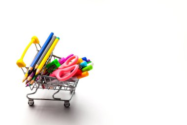 Beyaz arka planda izole edilmiş çok renkli okul malzemeleriyle dolu bir alışveriş arabası. Okul konseptine dönelim.