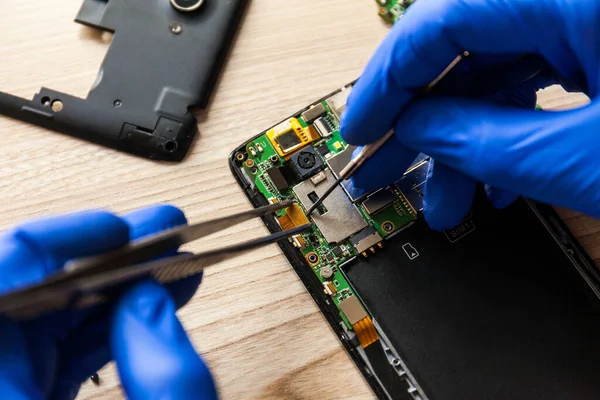 The technician repairing the smartphones motherboard in the workshop on the table. Concept of mobile phone, electronic, upgrade and technology.