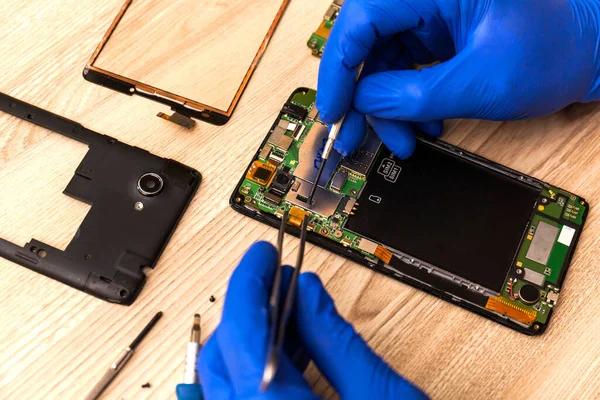 The technician repairing the smartphones motherboard in the workshop on the table. Concept of mobile phone, electronic, upgrade and technology.