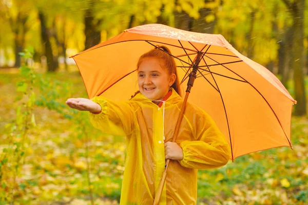 Happy child in the rain. Funny kid playing outdoors and catching rain drops in Autumn park