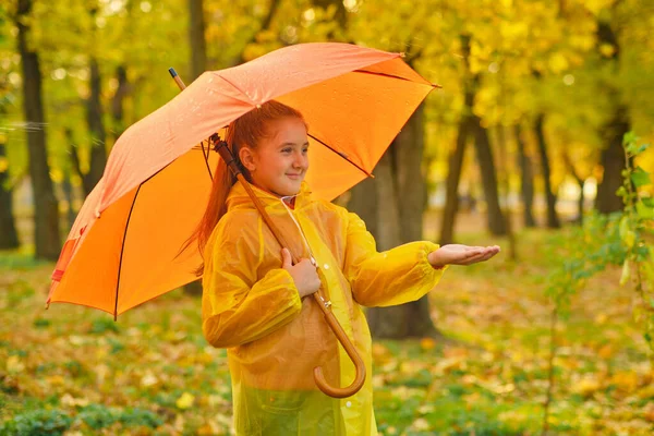 Happy child in the rain. Funny kid playing outdoors and catching rain drops in Autumn park