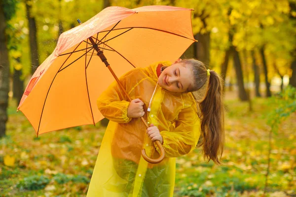 Happy child in the rain. Funny kid playing outdoors and catching rain drops in Autumn park