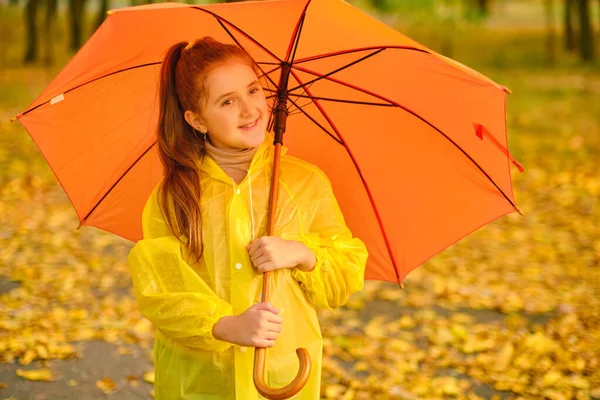 Happy child in the rain. Funny kid playing outdoors and catching rain drops in Autumn park