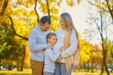 Genç bir aile, oğullarıyla birlikte dinleniyorlar, sonbahar güneşli parkta oturuyorlar, mutlu, birlikte gülümsüyorlar..