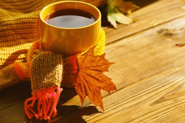 Sonbahar arkaplanı - sıcak eşarplı bir fincan çay ve ahşap masada yumuşak güneş ışığı altında kuru sonbahar yaprağı. Sonbahar zamanını rahat evde geçirme kavramı, kopyalama alanı