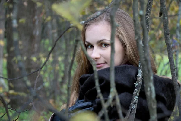 Kvinnan i svart päls titta igenom höstens grenar — Stockfoto