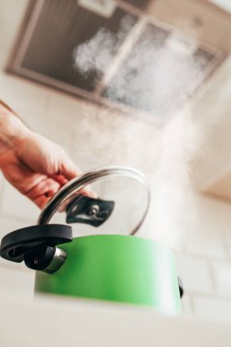 Ocaktaki yeşil tavanın kapağının altından çıkan kalın buhar yemek pişirmek için kaynar su.