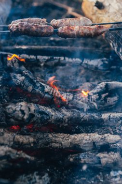 Kazıkta bir şişte kırsal sosis. Sosisler ormanda açık bir ateşte kızarır. Kamp yemeği.