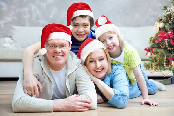 Amistosa familia en Santa Caps mirando a la cámara en la noche de Navidad —  Fotos de Stock