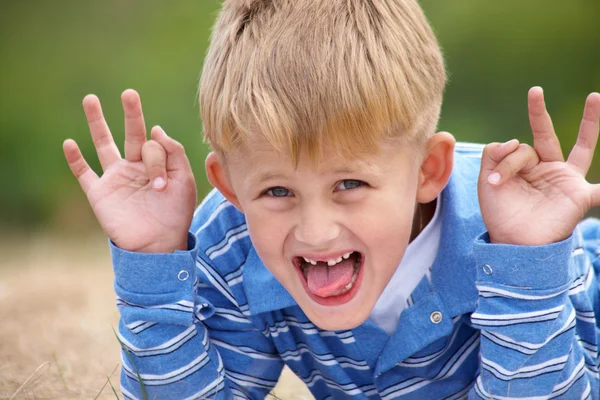 Мальчик строит веселые лица на фоне зеленых лугов — стоковое фото