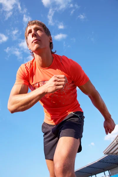 Jonge gespierde atleet loopt op het stadion achtergrond van de blauwe hemel — Stockfoto