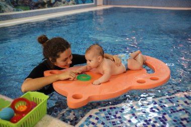 Yavru bebek, genç annesiyle havuzda yüzüyor.