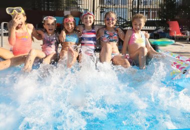 Çocuklar tatil köyünde havuzun kenarında su sıçratarak oyun oynarlar.