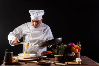 Beyaz üniformalı bir erkek aşçı, restoranda çalışırken servis etmeden önce tabakta sebzeli spagetti hazırlar.