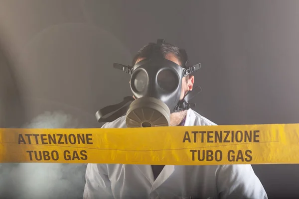 A medical engineer wearing antigas mask experienced in the gas leaks crisis directing the emergency during the chaos. On the yellow tape the written notice 