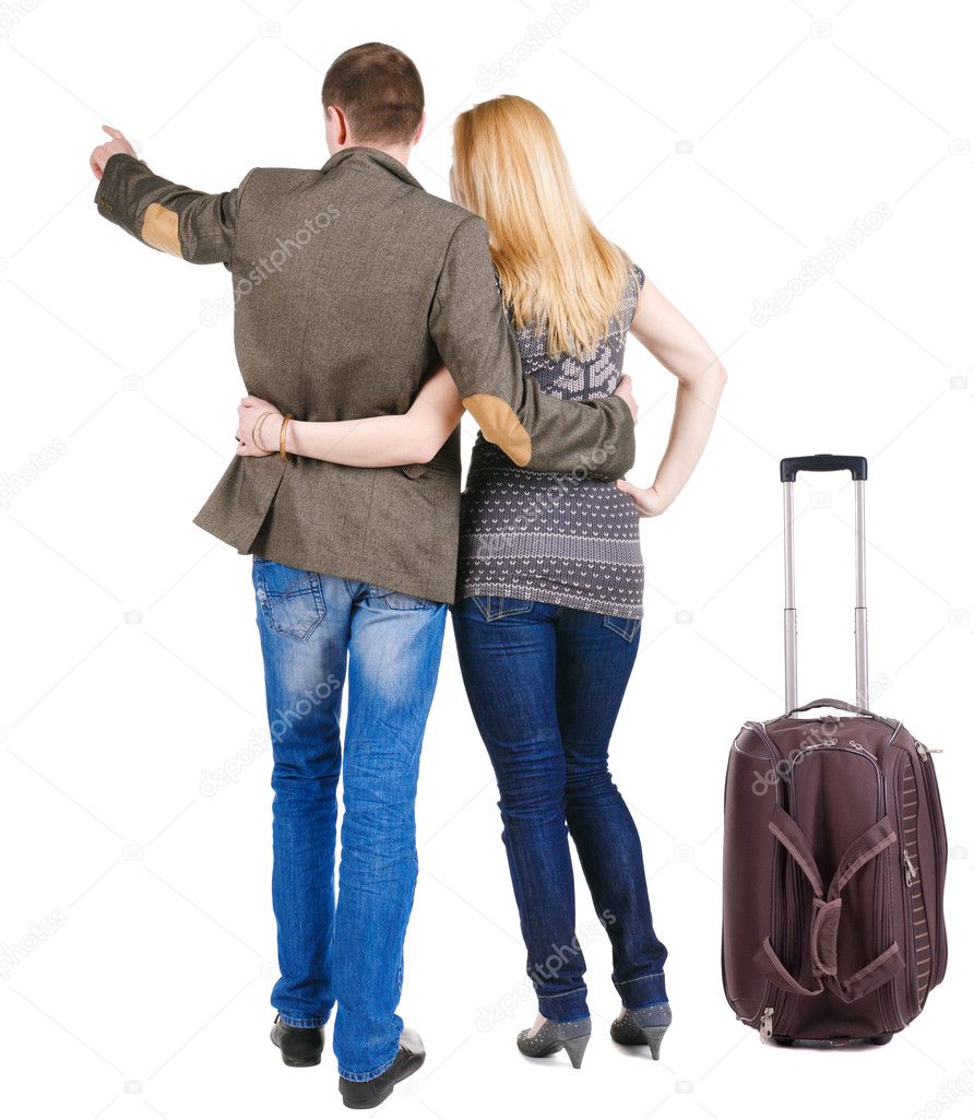 Back view of traveling young couple with suitcas pointing