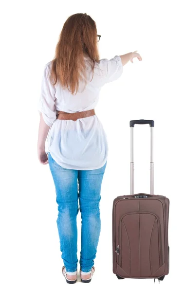 Traveling young woman with suitcas points at wall. — Stock Photo, Image